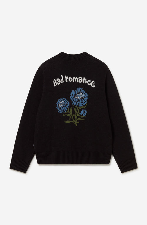 Jersey unisex de punto negro con cremallera, bordado Kaotiko Society en el pecho y gráfico jacquard de flores azules con mensaje Bad Romance en la espalda.